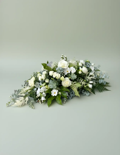 White Spray - A graceful and elegant funeral tribute designed to convey peace, love, and heartfelt remembrance. Created in a soothing palette of soft whites and fresh greenery, this casket spray offers a timeless expression of sympathy and respect. Its flowing, natural design symbolises purity, comfort, and the enduring memories shared with a loved one. Suitable for funeral services and celebrations of life, this arrangement provides a beautiful and dignified farewell, bringing a sense of calm and reflection to the occasion.