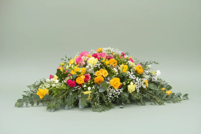 Vibrant Spray - A bright and uplifting funeral tribute designed to celebrate a life filled with love, kindness, and treasured memories. Featuring a radiant blend of warm and cheerful tones nestled among flowing greenery and delicate textures, this casket spray offers a heartfelt expression of remembrance and gratitude. Its natural, abundant design brings warmth and comfort to family and friends while honouring the unique spirit of a loved one. Suitable for funeral services, memorial ceremonies, and celebrations of life, this arrangement provides a beautiful and meaningful farewell.