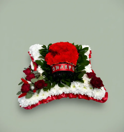 Boxing Glove - A distinctive funeral tribute featuring a traditional boxing glove design, thoughtfully arranged on a classic pillow-style base. Personalised with a name ribbon and presented in striking red, white, and black tones, this tribute offers a meaningful way to celebrate a loved one’s personality, interests, or heritage. Carefully crafted to convey respect, remembrance, and affection, it serves as a memorable focal point at funeral services, memorial ceremonies, or celebrations of life, honouring a unique individual with dignity and warmth.