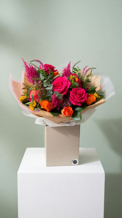 Cerise Inferno - Bold, vibrant and full of fiery colour, Cerise Inferno is a striking bouquet that brings together vivid cerise-pink roses, glowing orange roses and rich seasonal blooms, complemented by dramatic magenta textures and fresh eucalyptus foliage.

Beautifully wrapped in layers of kraft paper and delicate blush mesh, this eye-catching arrangement combines contemporary floristry with a wild, romantic feel. The contrast of hot pink and fiery orange creates a bouquet bursting with energy, personality and warmth.